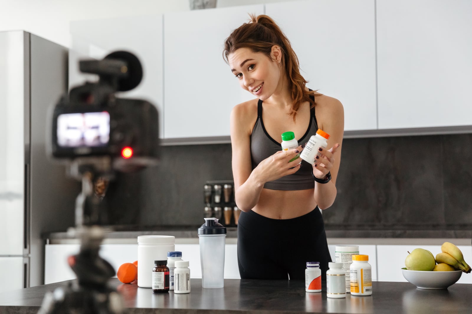 Creator filming a product video at home, holding supplement bottles